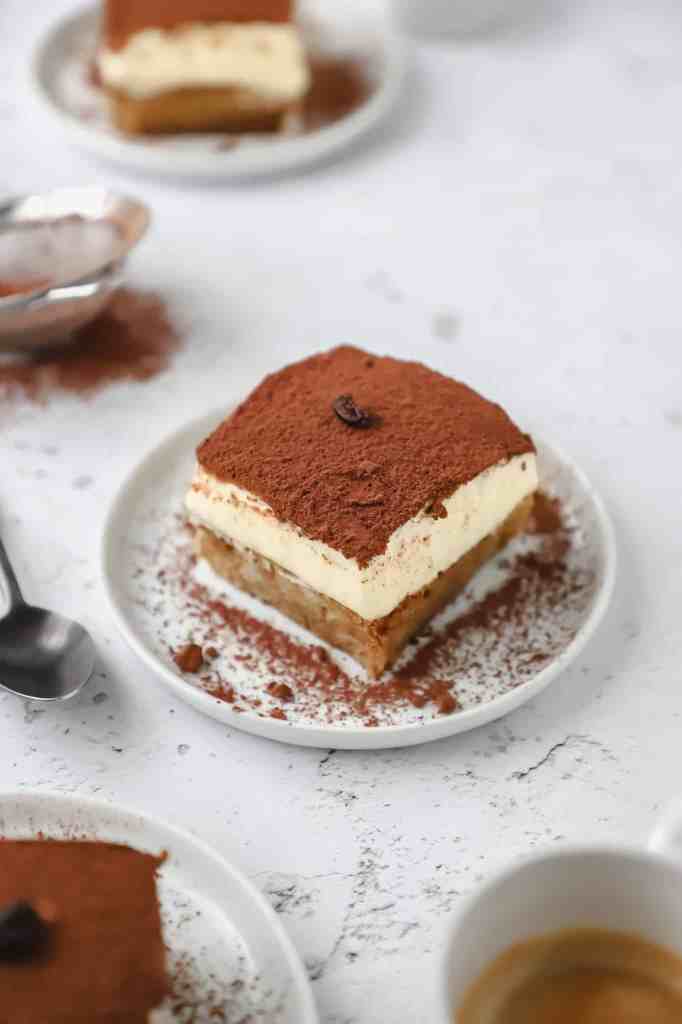 A single slice of authentic Italian tiramisu on a small white plate freshly dusted with cocoa powder